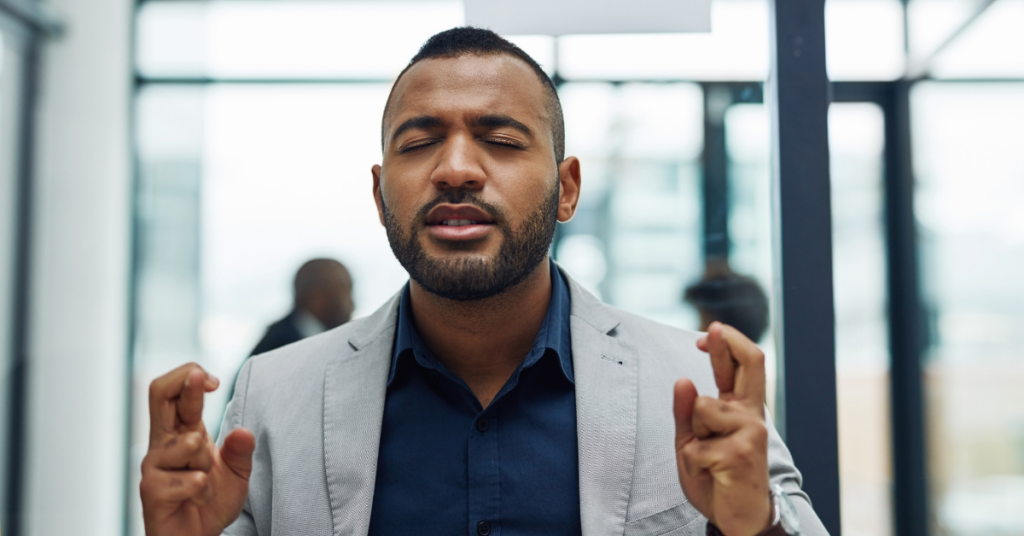 Man with eyes closed crossing fingers in an office space.